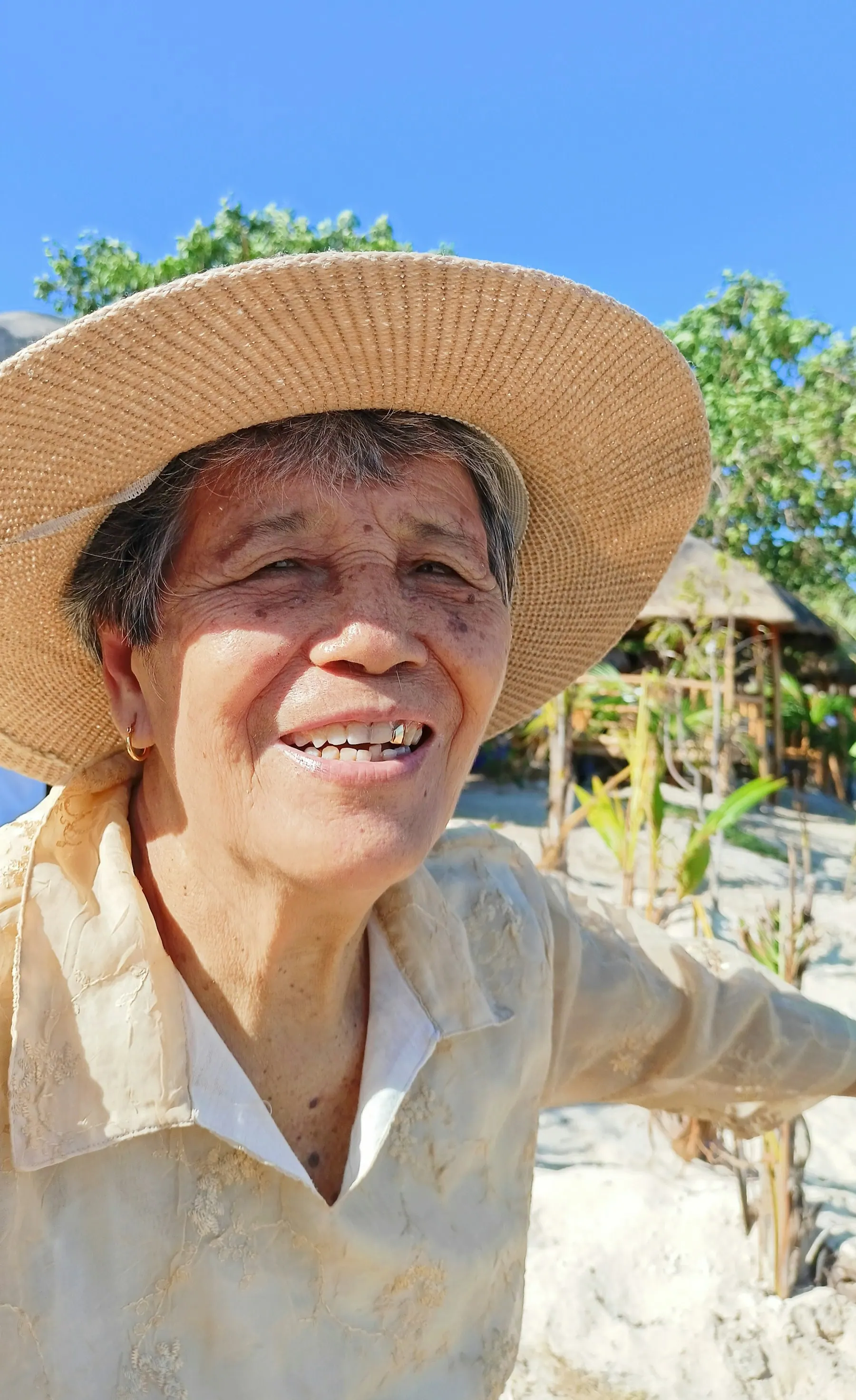 麦わら帽子をかぶり、日差しの中で笑う年配の女性